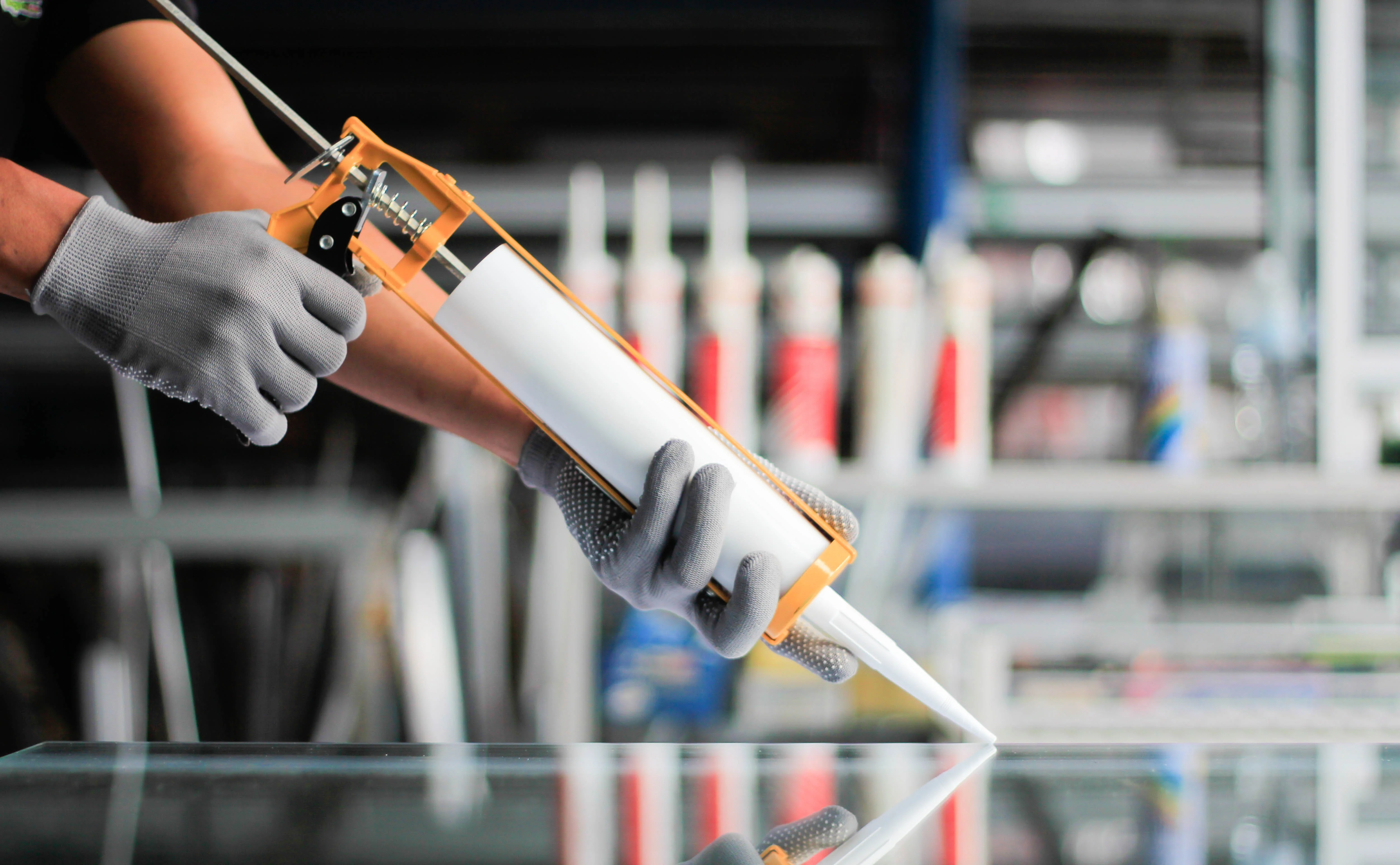 Professional adhesives and sealants application - worker using caulking gun with protective gloves in commercial setting